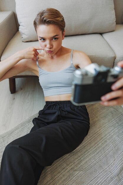 Vrolijke glimlach vrouw met een oude camera en het nemen van foto's van zichzelf als een weekendfotograaf in huiskleding met een kort kapsel haar zonder filters op een witte achtergrond gratis kopie ruimte