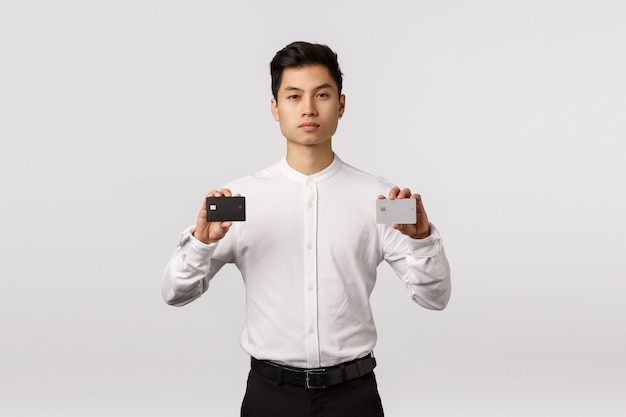 Vrolijke glimlachende Aziatische jonge ondernemer met de witte creditcards van de overhemdsholding