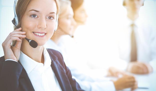 Vrolijke glimlachende zakenvrouw met koptelefoon die klanten raadpleegt. Groep diverse telefoonoperators aan het werk in zonnig kantoor. Callcenter en mensen uit het bedrijfsleven concept.