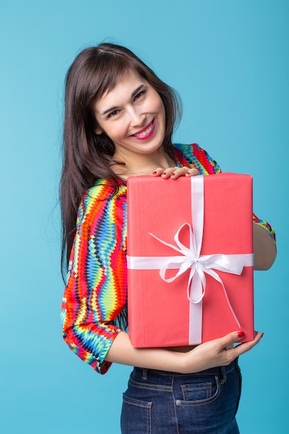 Vrolijke goed uitziende jonge brunette vrouw met een rode geschenkdoos in haar handen