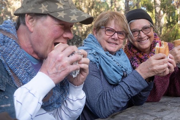 Vrolijke groep vrienden die buiten genieten van hun picknick terwijl ze een broodje eten en naar de camera kijken