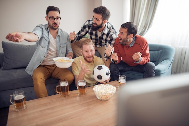 Vrolijke groep vrienden die voetbal op spel op TV letten