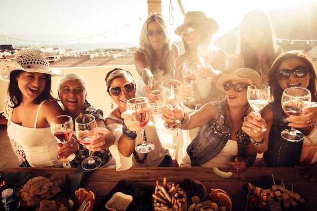 Vrolijke groep vrouwelijke mensen hebben samen plezier - vrienden roosteren met rode wijn buiten thuis - viering feestevenement voor mooie vrouwen lachen veel en glimlachen