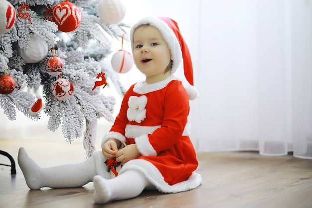 Vrolijke heldere kerst. Mooie baby geniet van Kerstmis. Jeugdherinneringen. Santa meisje klein kind vieren kerst thuis. Vakantie met het gezin. Meisje schattig kind vrolijke stemming spelen in de buurt van kerstboom.