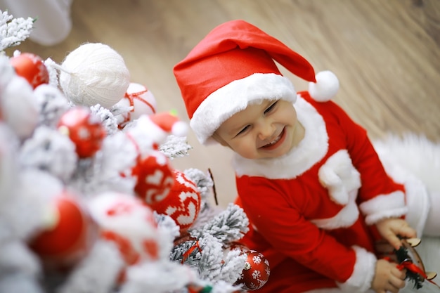 Vrolijke heldere kerst. Mooie baby geniet van Kerstmis. Jeugdherinneringen. Santa meisje klein kind vieren kerst thuis. Vakantie met het gezin. Meisje schattig kind vrolijke stemming spelen in de buurt van kerstboom.