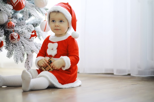 Vrolijke heldere kerst. Mooie baby geniet van Kerstmis. Jeugdherinneringen. Santa meisje klein kind vieren kerst thuis. Vakantie met het gezin. Meisje schattig kind vrolijke stemming spelen in de buurt van kerstboom.