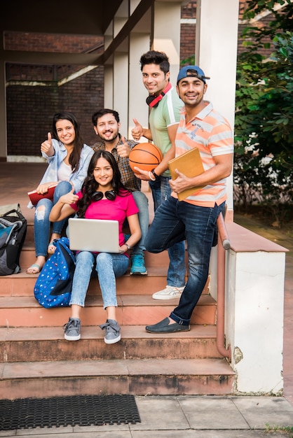 Vrolijke Indiase Aziatische jonge groep studenten of vrienden die samen lachen terwijl ze op de campus zitten, staan of lopen