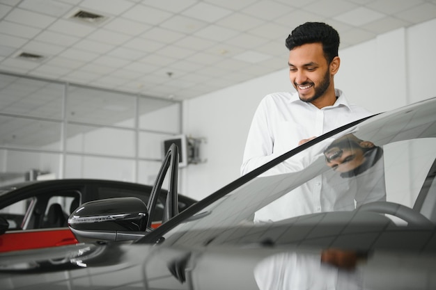 Vrolijke Indiase man die autokenmerken controleert in de showroom