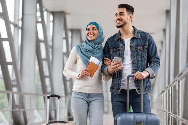 Vrolijke islamitische echtgenoten staan met bagagepaspoorten en smartphone op de luchthaven