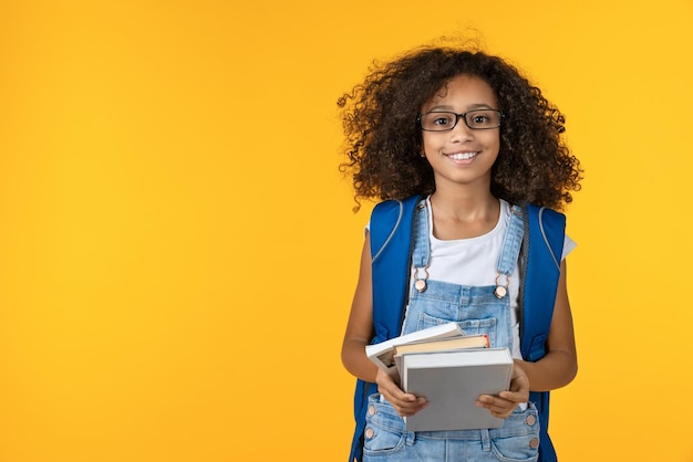 Foto vrolijke jonge afrikaanse meisjesjongen in brillen met notitieboekje en boeken voor studie