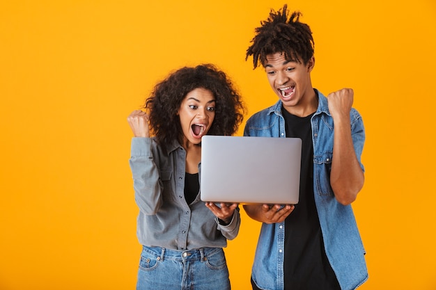 Vrolijke jonge Afrikaanse paar staande geïsoleerd, met laptop computer, vieren