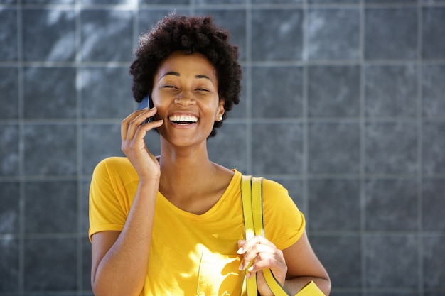 Vrolijke jonge Afrikaanse vrouw die een telefoongesprek maakt