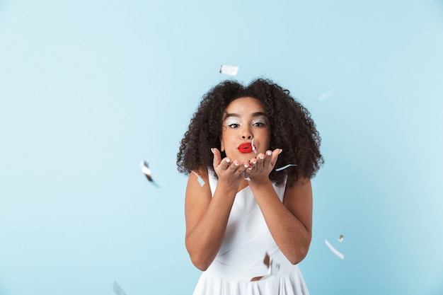 Vrolijke jonge Afrikaanse vrouw, gekleed in jurk vieren geïsoleerd, spelen met confetti