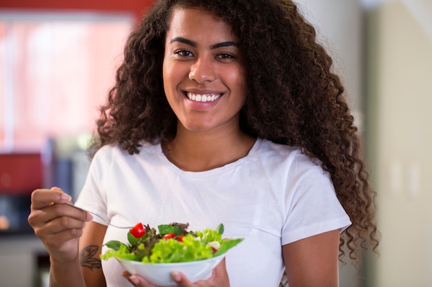 vrolijke jonge afro-Amerikaanse vrouw die groentesalade in huiskeuken eet