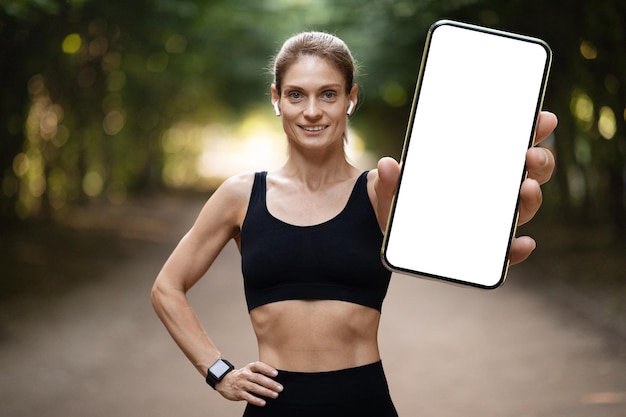 Vrolijke jonge atletische vrouw die smartphonemodel toont