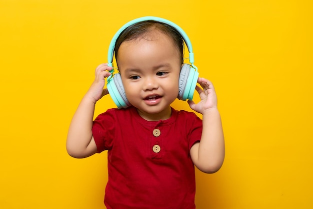 Vrolijke jonge Aziatische jongen 2-jarige babyjongen in rode tshirt luisteren naar favoriete muziek met koptelefoon geïsoleerd op gele achtergrond Moederdag liefde familie lifestyle concept