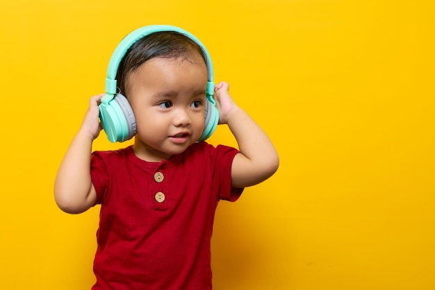 Vrolijke jonge Aziatische jongen 2-jarige babyjongen in rode tshirt luisteren naar favoriete muziek met koptelefoon geïsoleerd op gele achtergrond Moederdag liefde familie lifestyle concept