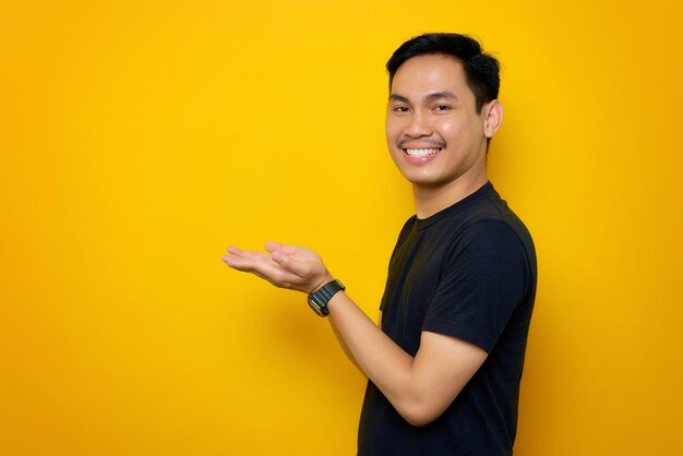 Vrolijke jonge Aziatische man in casual t-shirt met kopieerruimte op palm geïsoleerd op gele achtergrond Geweldig aanbod concept