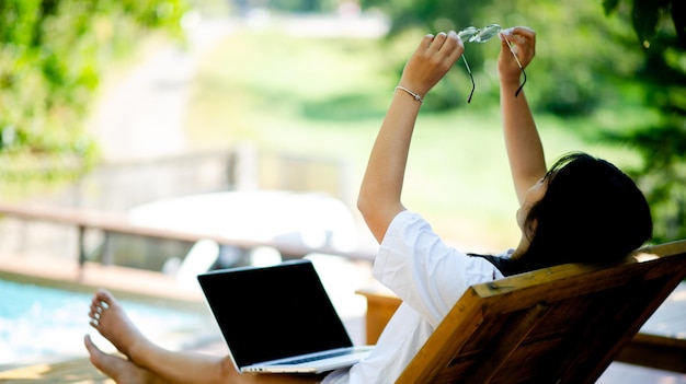 Vrolijke jonge aziatische vrouw die lacht terwijl ze op haar laptop buiten het kantoor thuis werkt, thuis in het park werkt, thuis werkt en online werkt