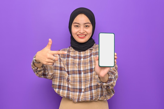 Vrolijke jonge Aziatische vrouw in geruit hemd met een leeg scherm mobiele telefoon geïsoleerd op paarse achtergrond