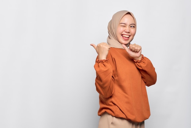 Vrolijke jonge Aziatische vrouw in oranje shirt wijzende vingers naar kopieerruimte geïsoleerd op witte achtergrond