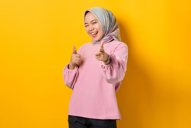 Vrolijke jonge Aziatische vrouw in roze shirt wijzende vingers op camera op gele achtergrond