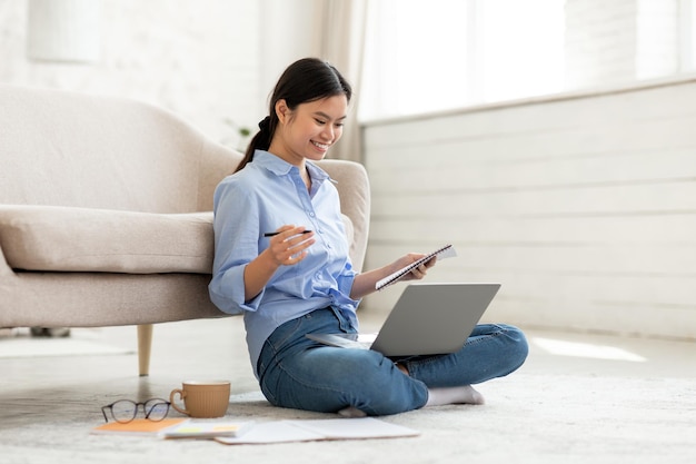 Vrolijke jonge Aziatische vrouw zittend op de vloer met laptop