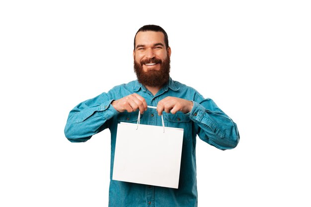 Vrolijke jonge bebaarde man houdt witte boodschappentas met kopie ruimte
