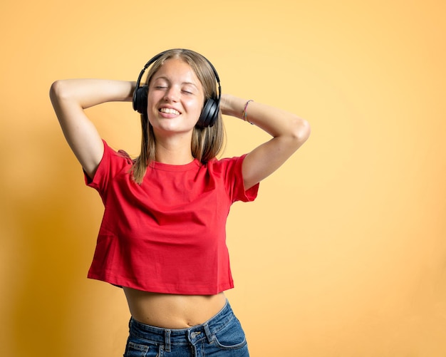 Vrolijke jonge blonde vrouw muziek luisteren met draadloze koptelefoon, dansen en plezier maken, mensen entertainment en hobby concept, levendige oranje achtergrond, rood t-shirt en blu jeans
