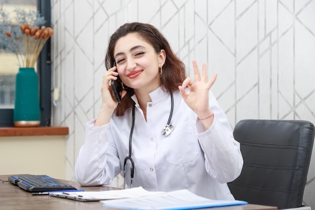 Vrolijke jonge dokter die oin de telefoon praat en gebaart ok hoge kwaliteit foto