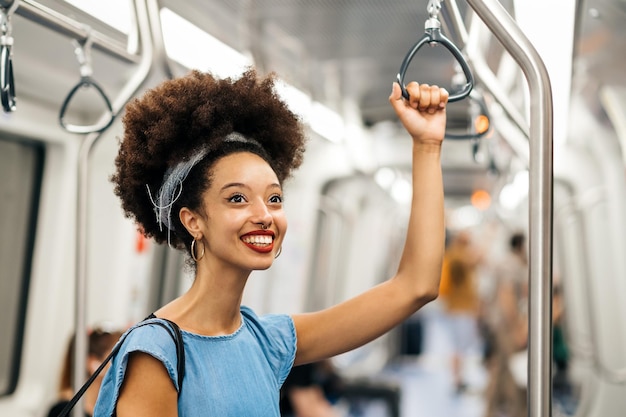 Vrolijke jonge etnische vrouw die het handvat vasthoudt tijdens het rijden in de metro