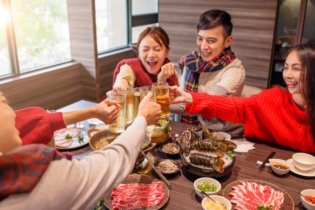 Vrolijke jonge groep die bier roostert in het hot pot restaurant