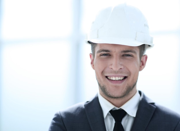 Vrolijke jonge ingenieur is klaar om te werken De man kijkt naar de camera en glimlacht Hij draagt een witte helm