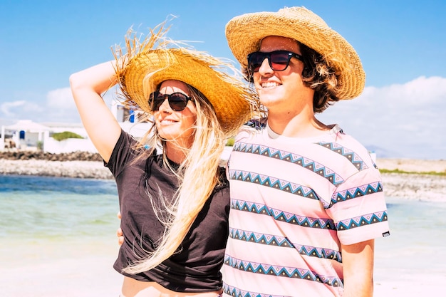 Vrolijke jonge jongen en meisje glimlachen samen op het strand in zomertoerisme vakantie vakantie strohoeden reizen paar met zon op gezicht gelukkige mensen in relatie buiten vrijetijdsbesteding en plezier