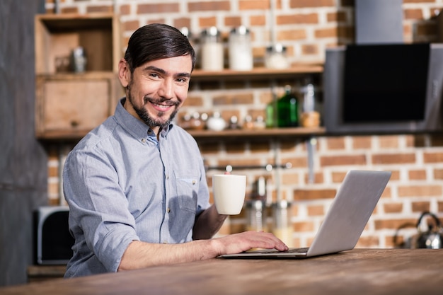 Vrolijke jonge knappe man koffie drinken tijdens het online werken