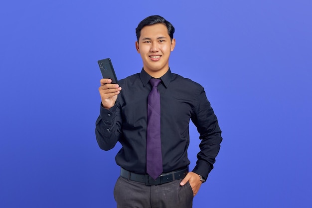 Vrolijke jonge knappe zakenman die smartphone vasthoudt en naar camera kijkt op paarse achtergrond
