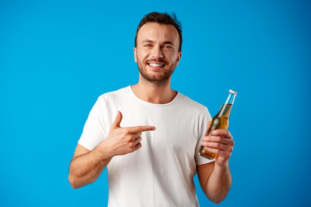 Vrolijke jonge man in t-shirt met bierflesje tegen blauwe achtergrond