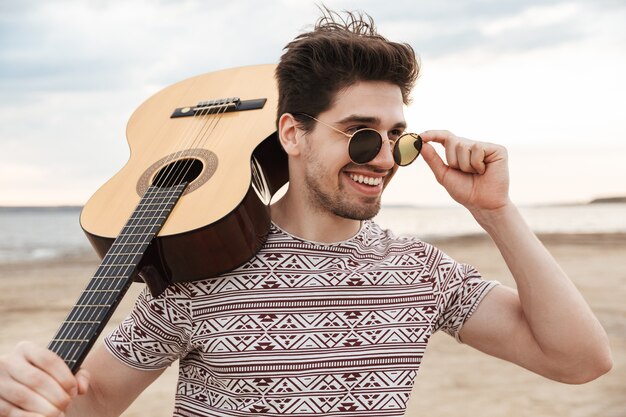 Vrolijke jonge man met gitaar, staande op het strand