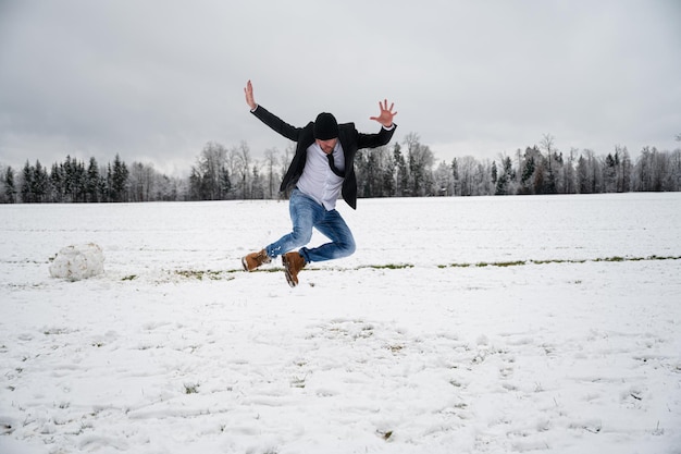 Vrolijke jonge man opgewonden springend in de lucht buiten in een besneeuwde natuur.