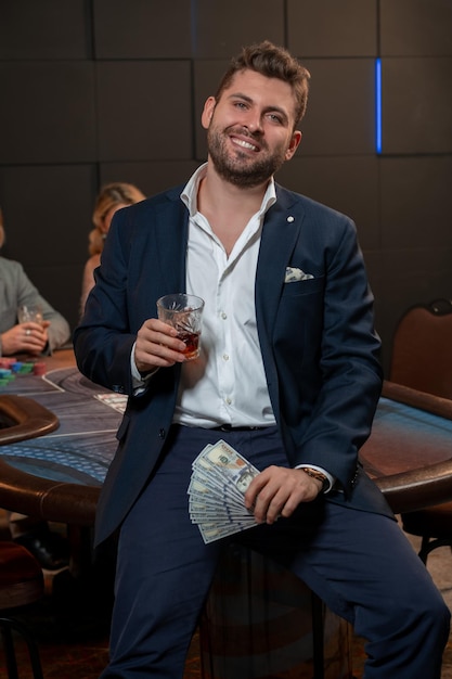 Vrolijke jonge man viert overwinning in pokerspel met glas whisky
