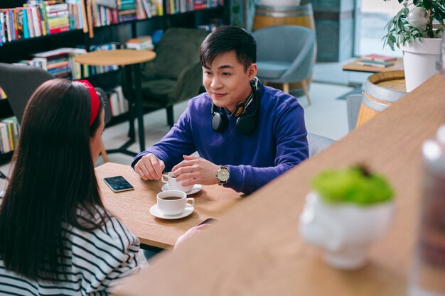 Vrolijke jonge man zit met een kopje koffie en kijkt naar de jonge vrouw voor hem