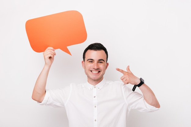 Vrolijke jonge mens die een dialoogwolk of een rechthoekige oranje bellentoespraak op witte achtergrond houden.