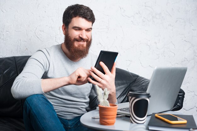 Vrolijke jonge mensenzitting in bureau en het gebruiken van tablet