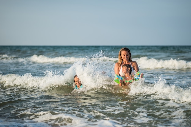 Vrolijke jonge moeder zwemt in de zee met haar charmante dochtertjes en geniet van het langverwachte weekend op een zonnige zomerdag. Concept familievakantie.