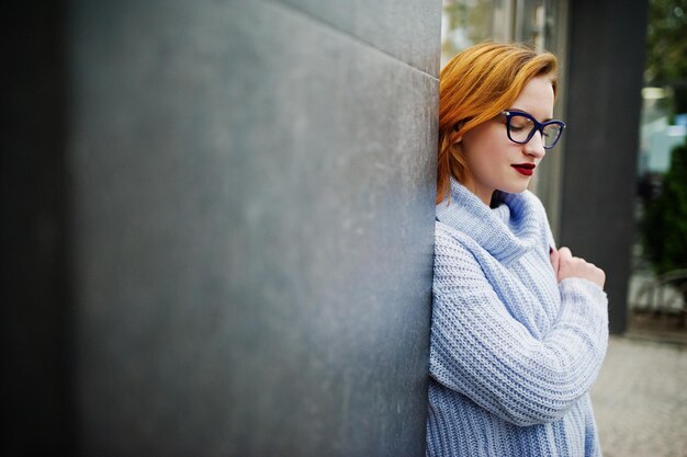 Vrolijke jonge mooie roodharige vrouw in glazen warme blauwe wollen trui met rugzak buiten geposeerd