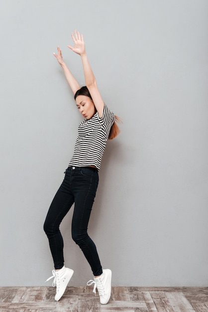 Vrolijke jonge mooie vrouw dansen over grijze muur