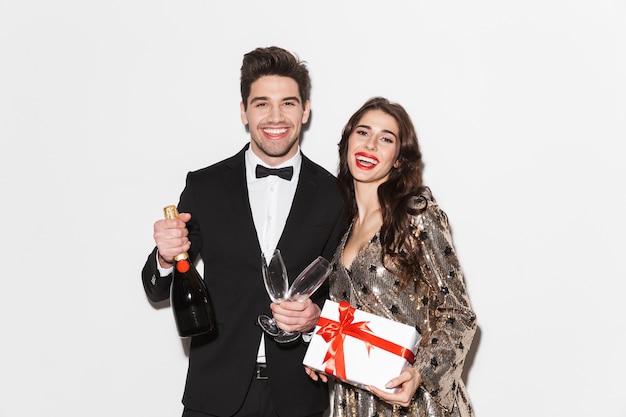 Vrolijke jonge netjes geklede paar vieren nieuwjaarsfeest geïsoleerd over wit, met huidige doos, champagne met ywo glazen