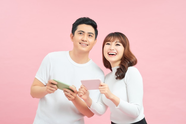 Vrolijke jonge paar man en vrouw glimlachen en verheugen zich tijdens het spelen van videogames op mobiele telefoons geïsoleerd op gele achtergrond