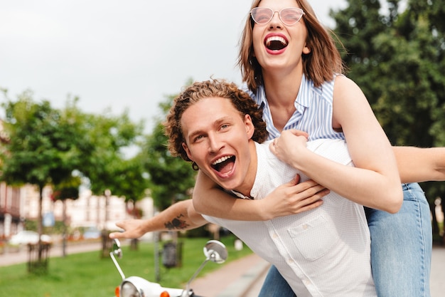 Vrolijke jonge paar plezier samen met scooter en kijken naar de camera terwijl ze in het park