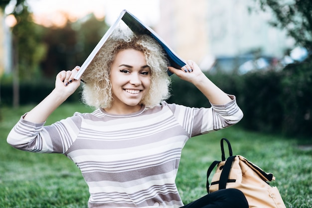 Foto vrolijke jonge studentenmeisje houdt het boek over haar hoofd en glimlacht